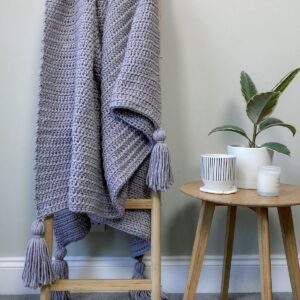 A modern crochet blanket used as home decor hung over a ladder